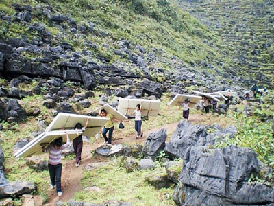 女村民在崎岖的山路上扛材料进村建校